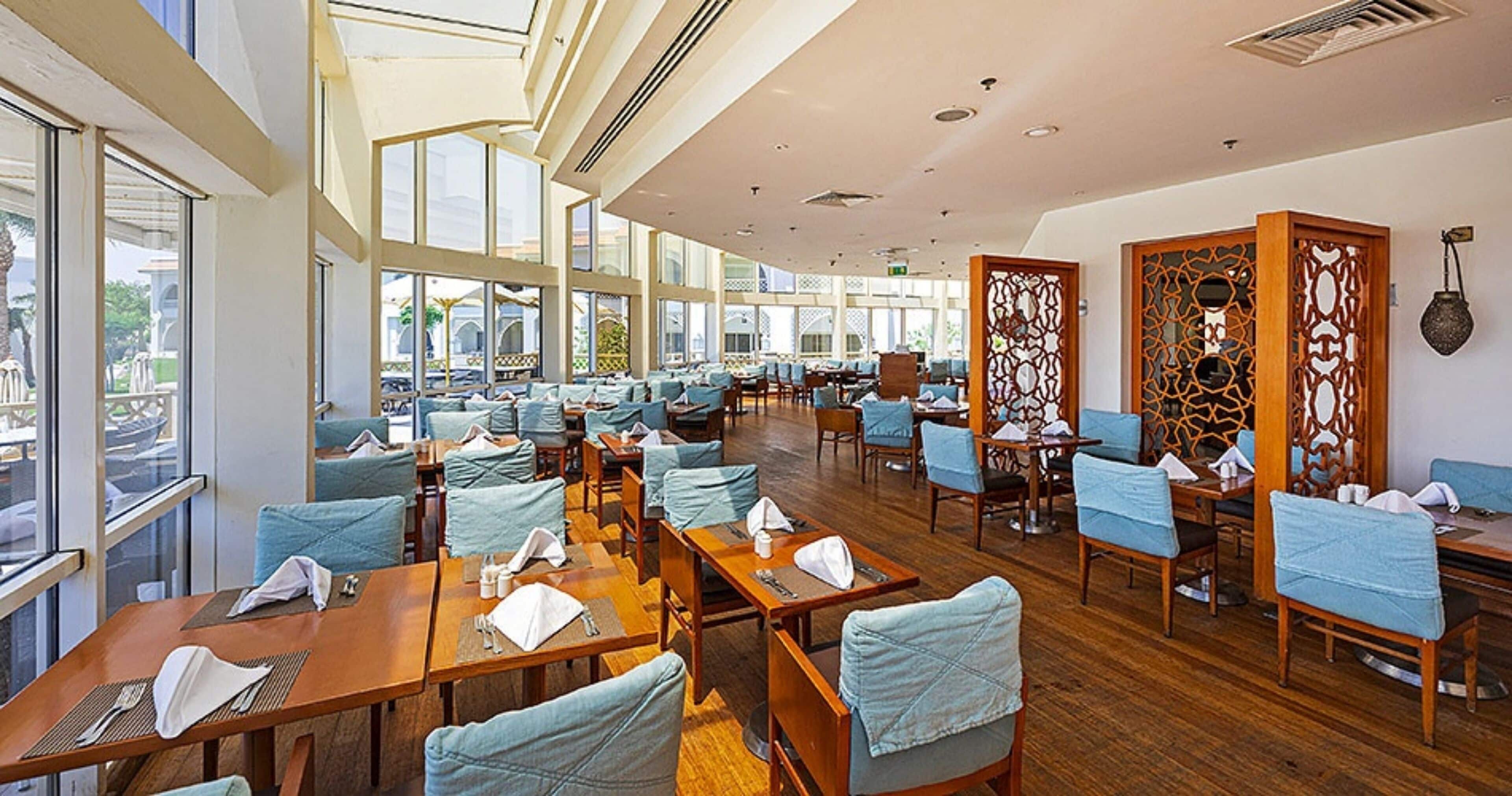 A spacious indoor dining area with multiple tables and chairs, large windows, and a decorative partition.