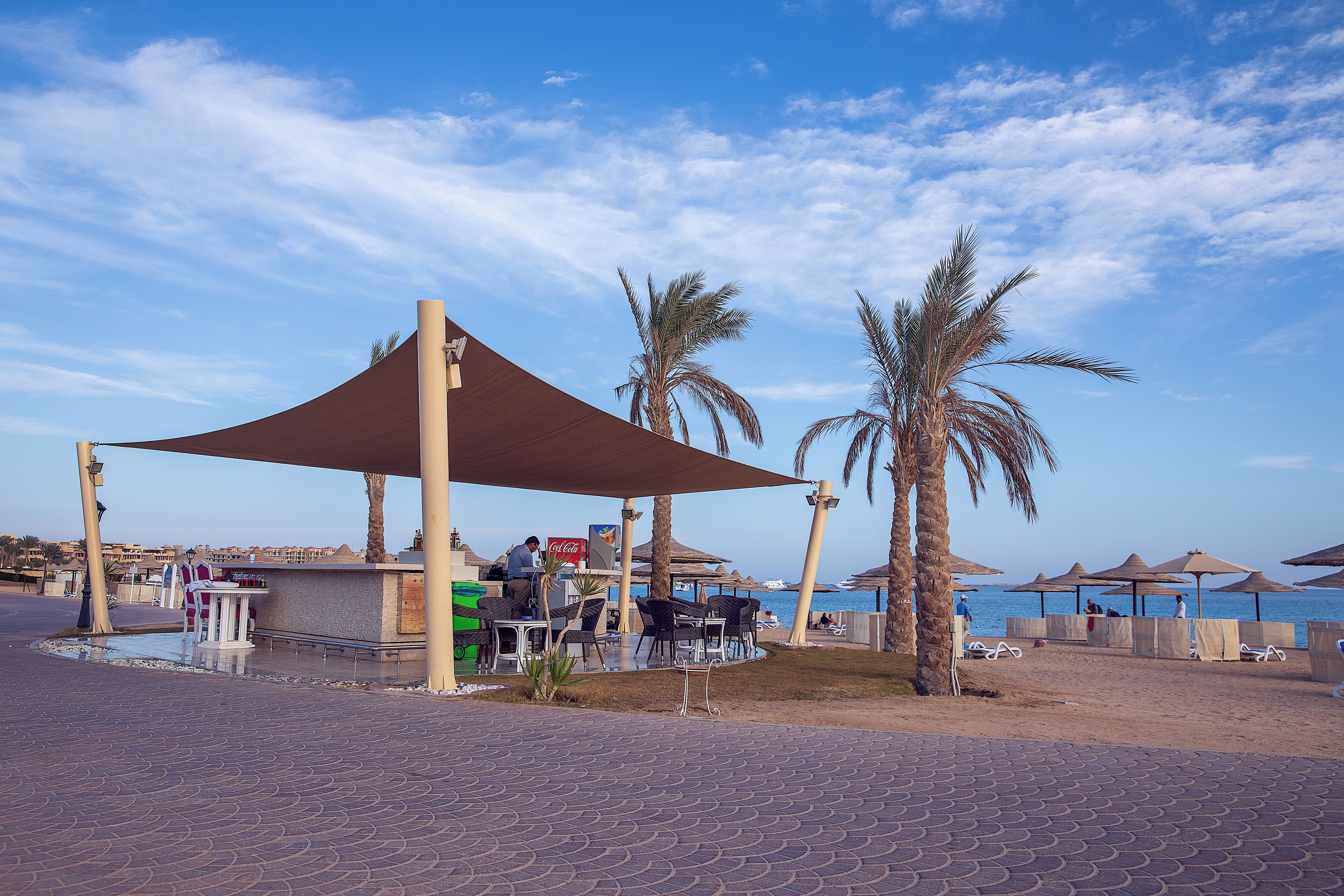 A beachside café with outdoor seating, palm trees, and a view of the sea.