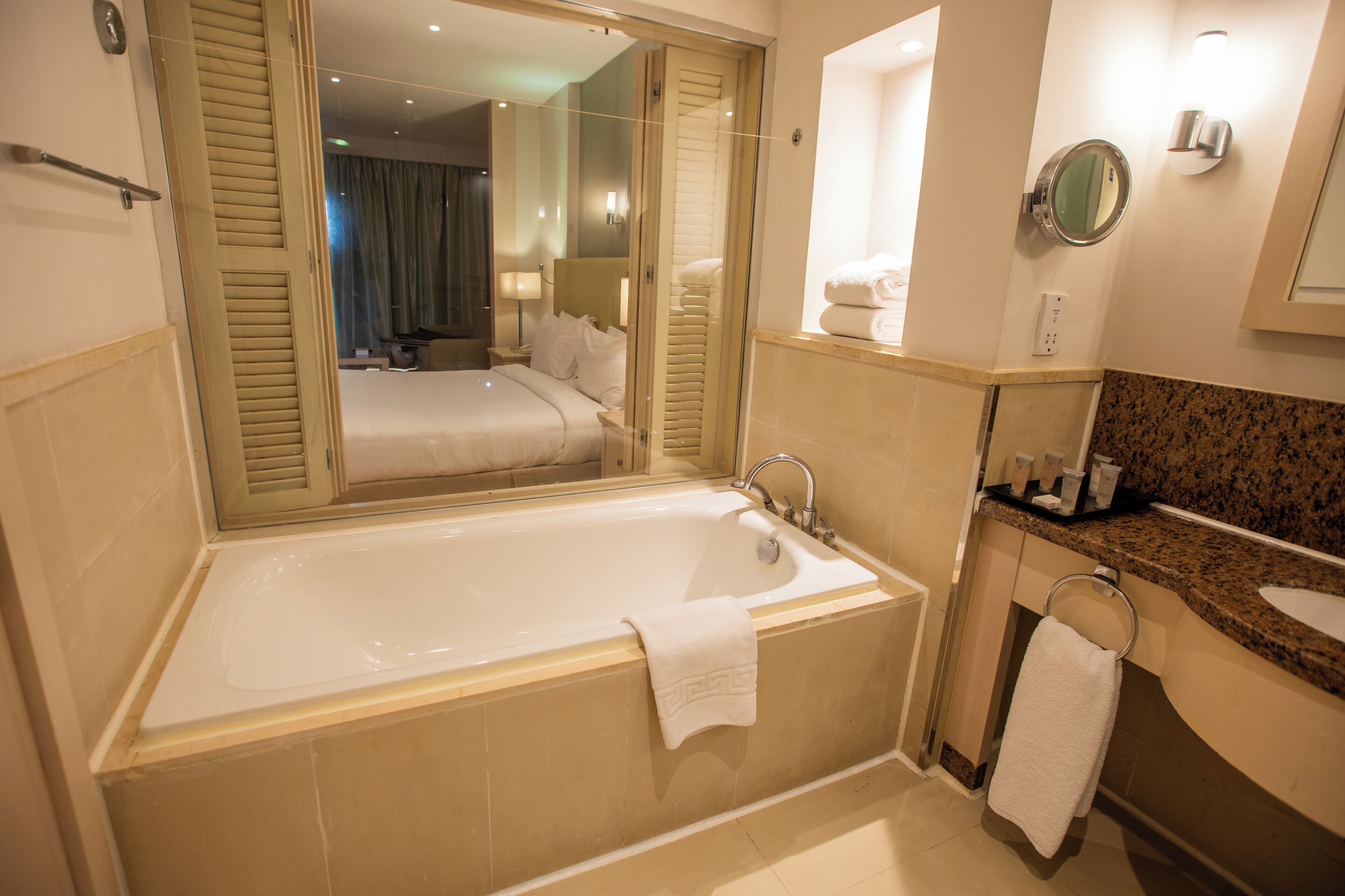 A hotel bathroom with a large bathtub, a mirror, a sink, and a vanity with toiletries.
