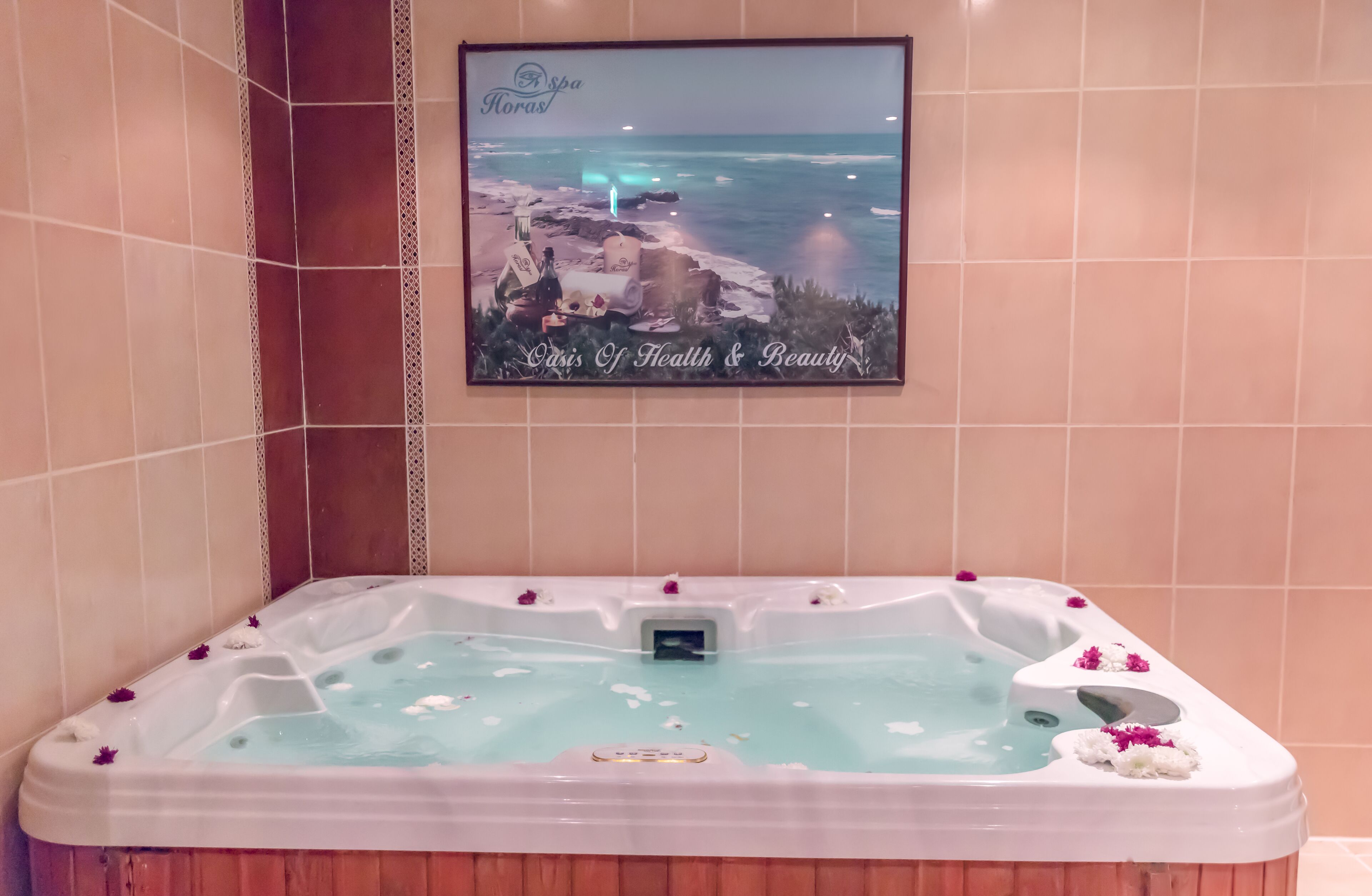 A spa area with a framed picture of a beach, a hot tub with flowers, and a control panel.