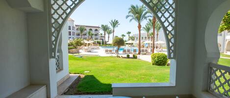 A view from a covered outdoor area with a glass table and chairs, overlooking a pool and palm trees.