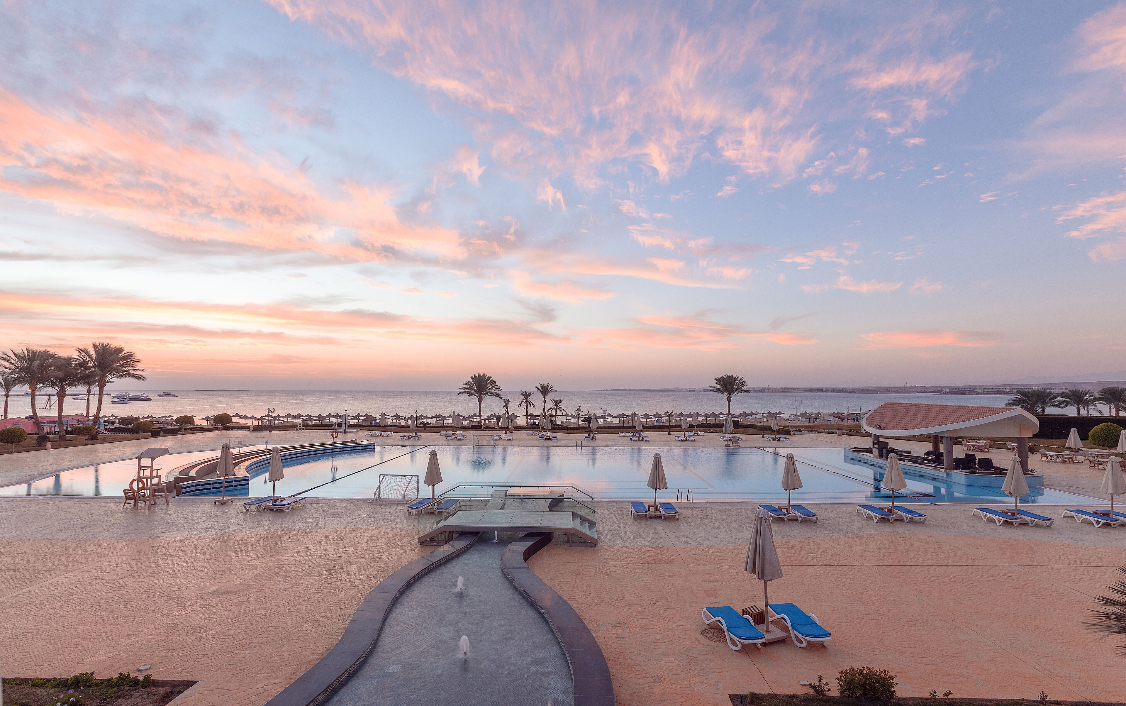 A resort pool area with sun loungers, umbrellas, and a water feature.