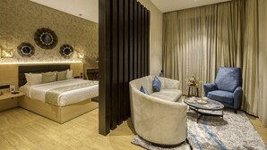 A modern hotel room with a large bed, a curved armchair, a small round table, and a blue armchair. - Le Foliage by TGI (Bengaluru)