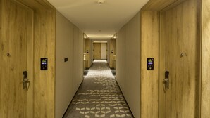 A hotel hallway with wooden doors, numbered room signs, and a patterned carpet. - Le Foliage by TGI (Bengaluru)