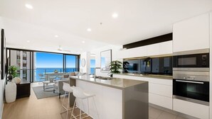 A modern kitchen with a large island, stainless steel appliances, and a view of the sea.