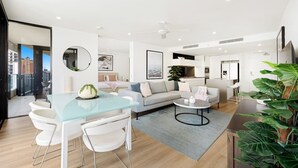 A modern living room with a glass dining table, white sofas, and a large plant.