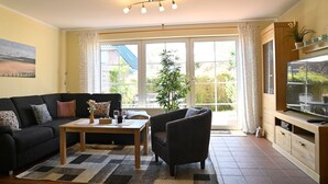 A living room with a sofa, armchair, coffee table, and a TV on a wooden cabinet. - Dirks Ferienhaus Fleute - Holiday home Fleute (Varel)