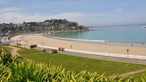 A coastal beach with a white fence, a paved walkway, and a view of the sea and buildings in the background. - Charming Cottage with WIFI, 150m from Town Center, 750m to Beach (Perros-Guirec)