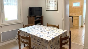 A dining area with a table covered in a nautical-themed tablecloth, a television on a wooden stand, and a poster of marine life on the wall.