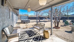 Une terrasse extérieure dotée d’un espace salon couvert, d’un banc en osier, d’un tapis à motifs et d’un luminaire suspendu.