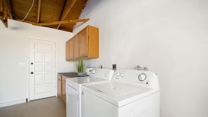 Une buanderie équipée d’un lave-linge et d’un sèche-linge à chargement frontal, de meubles en bois, d’une porte et d’un plafond avec des poutres apparentes.
