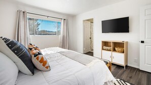 Une chambre à coucher avec un lit, une télévision, une armoire et une fenêtre avec des rideaux.