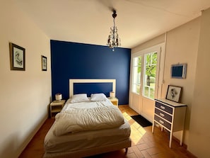 A bedroom with a bed, bedside tables, a dresser, a chandelier, and framed pictures on the walls.