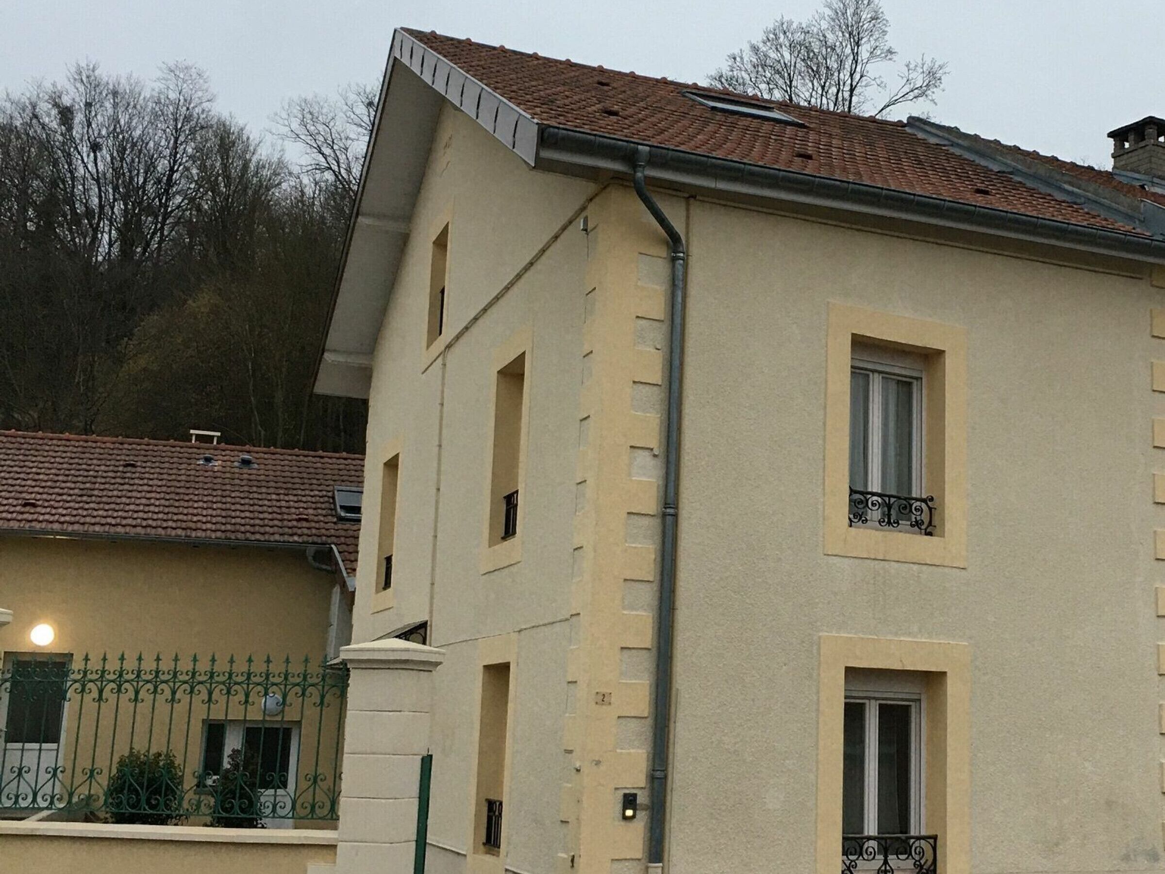 A two-story building with a beige facade, a red-tiled roof, and a small balcony with a wrought iron railing.