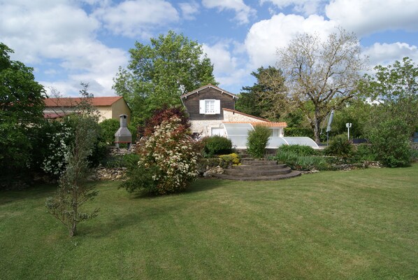 A house with a red roof, surrounded by a well-maintained garden with various plants and a lawn.