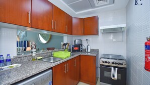 A compact kitchen with wooden cabinets, a built-in washing machine, a microwave, and a gas stove. - Lake View Brand New Studio in X1 Tower JLT - LND (Dubai)