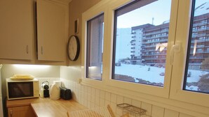 A kitchen with a microwave, toaster, and a window with a view of a snowy landscape and a building. - Tignes: Classic Apartment with Lake View, 5 Sleeps (Tignes)