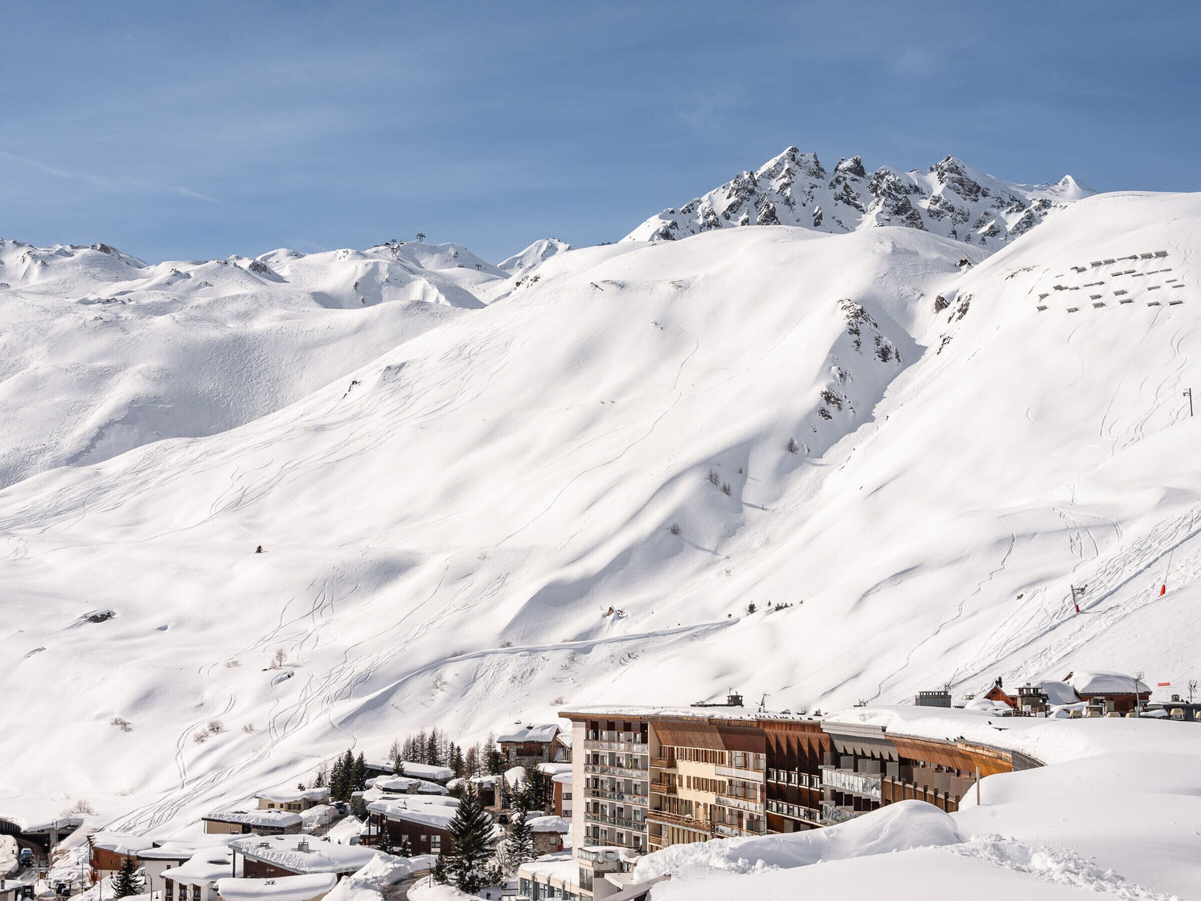 A snow-covered mountain landscape with a modern hotel building featuring multiple floors and balconies, situated at the base of the mountain.
