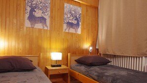 A room with two beds, wooden walls, and two wall-mounted lamps. - Tignes: Classic Apartment with Lake View, 5 Sleeps (Tignes)