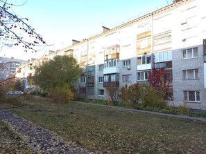 A multi-story residential building with balconies, a paved pathway, and surrounding vegetation. - Apartment on Zavodskaya 1 (Tyumen)