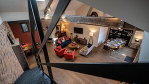 A spacious living area with a high ceiling, wooden flooring, and a dining table set for six.