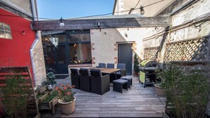 A wooden deck with outdoor seating, a red wall, and a building with a dark door.