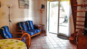 Een woonkamer met een bank, stoelen, een tafel, een televisie en een deur naar buiten.