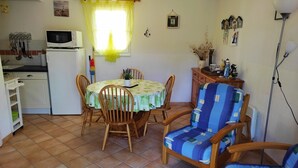 Een kleine keuken met een magnetron, spoelbak en kastjes. Een eettafel met stoelen staat in het midden.