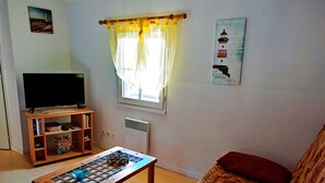 Een woonkamer met een tv op een houten standaard, een schaaktafel, een bank en een raam met gordijnen.
