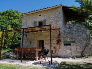 Un edificio de piedra con un porche cubierto, mobiliario exterior y una parrilla.