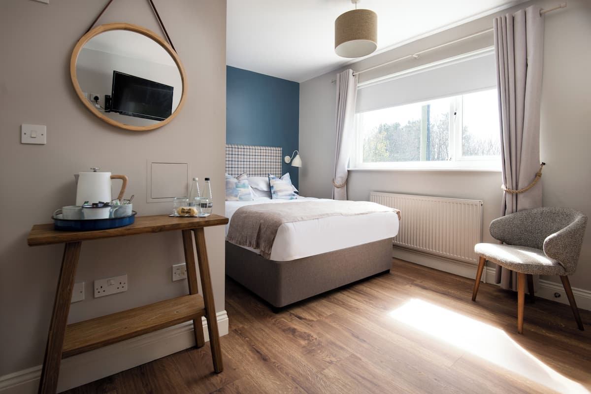 A bedroom with a bed, bedside table, chair, window, and a mirror.