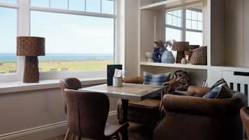 Una habitación con vista al mar, una mesa con sillas, un sofá de cuero marrón y estantes con objetos decorativos.