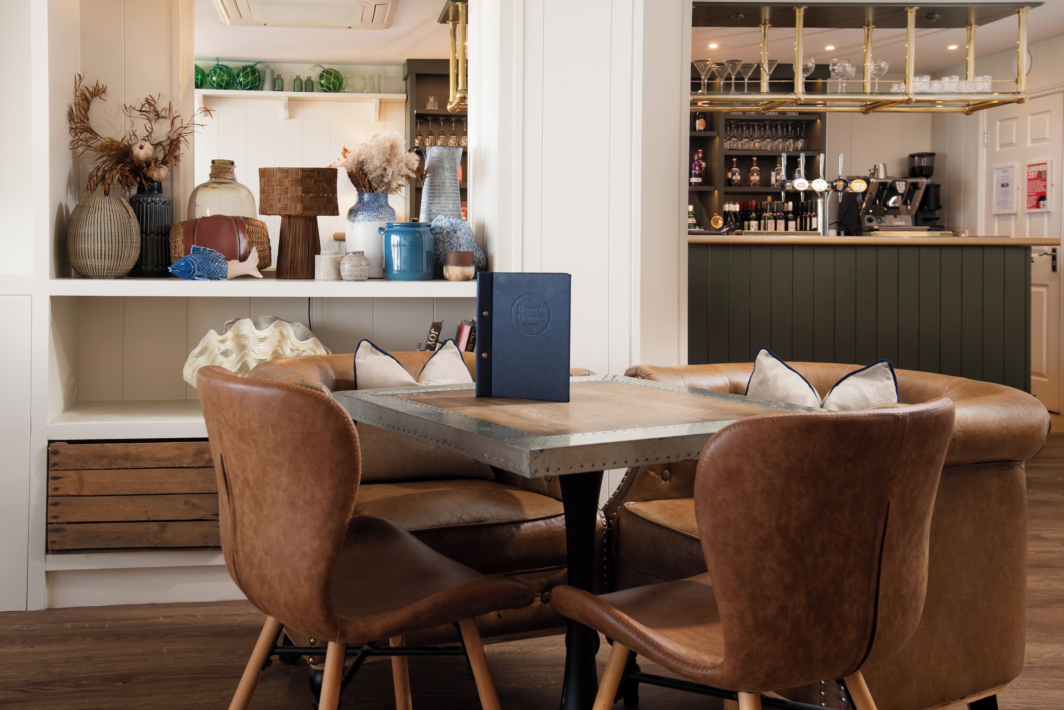 Un comedor con una mesa de madera, sillas de cuero y una zona de bar con estantes llenos de botellas y vasos.