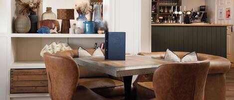 A dining area with a wooden table, leather chairs, and a bar area with shelves of bottles and glasses.