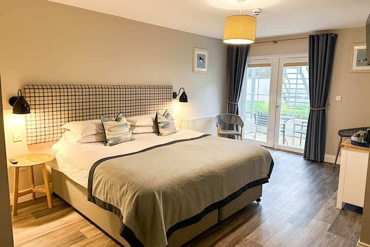 A bedroom with a large bed, bedside lamps, a chair, and a view of the outdoors.