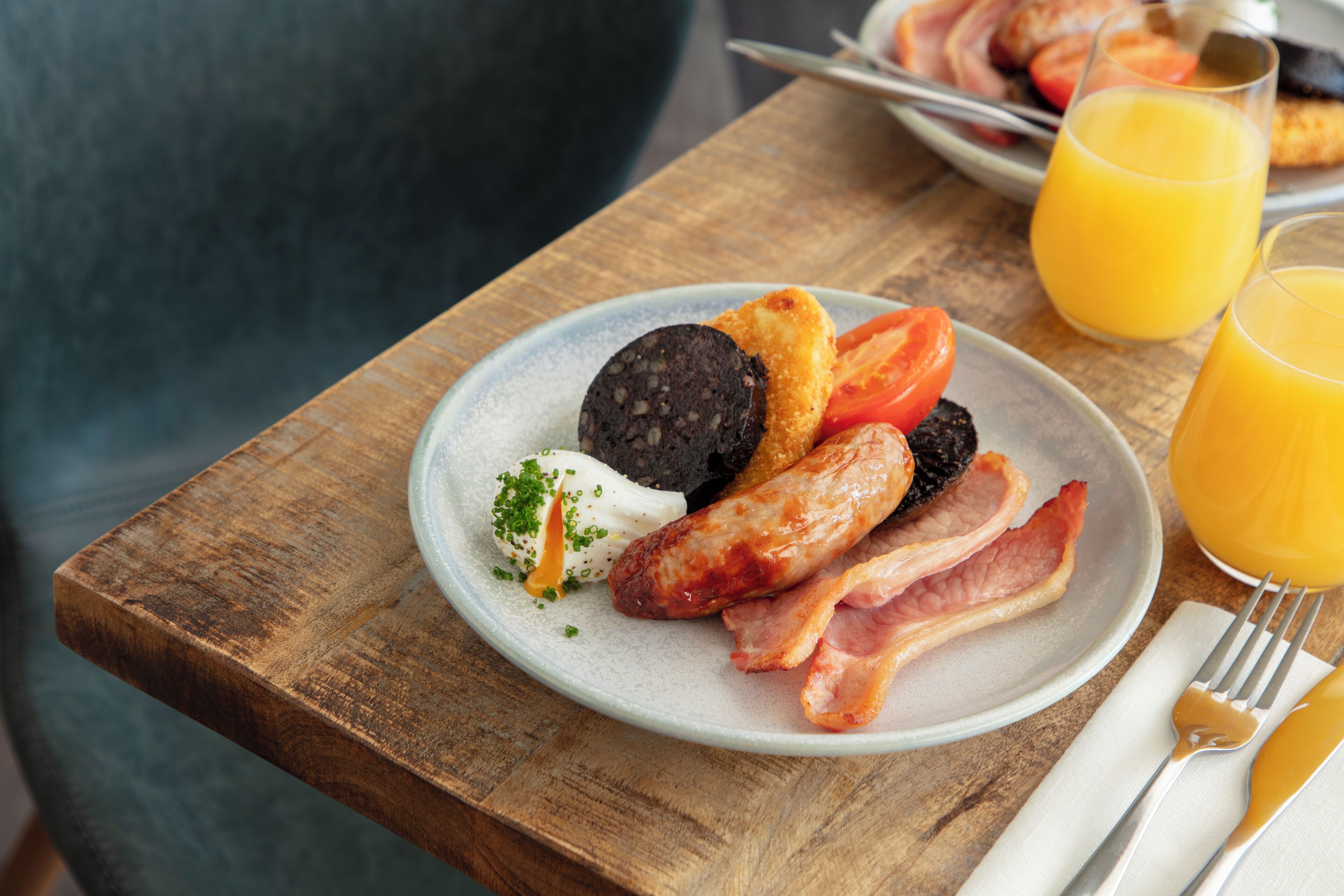 A breakfast plate with sausages, bacon, and a black pudding on a wooden table.