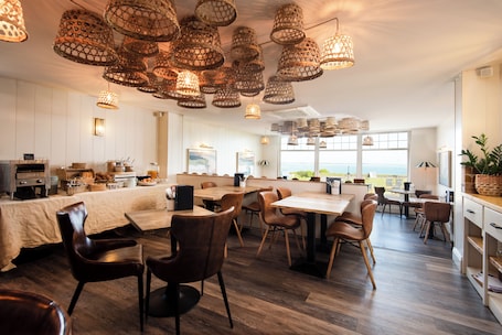 A modern kitchen with wooden cabinets, a dining area with a large table and chairs, and a view of the ocean.. Beach House Hotel