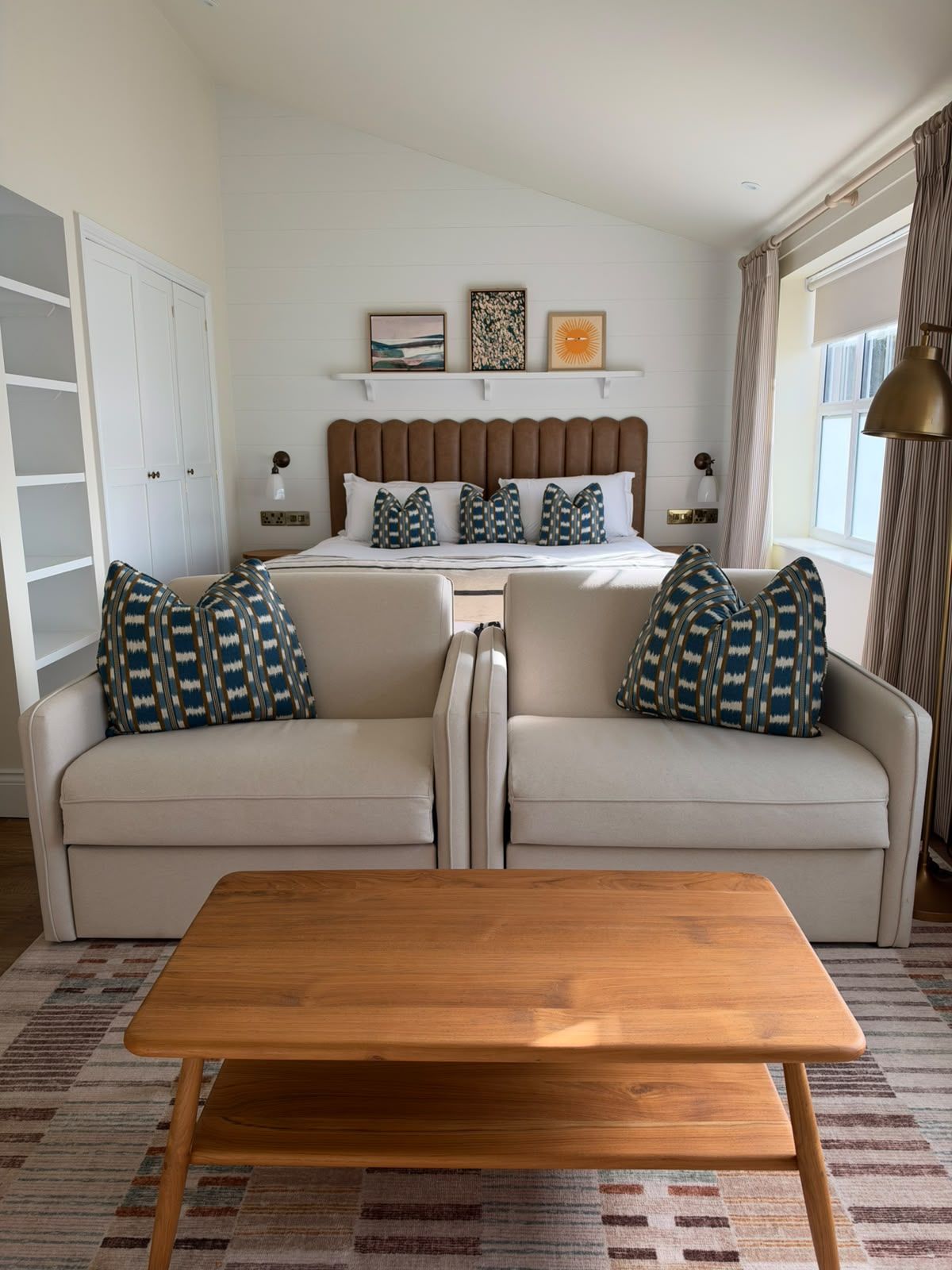 A bedroom with a bed, two sofas, a wooden table, and a window with curtains.