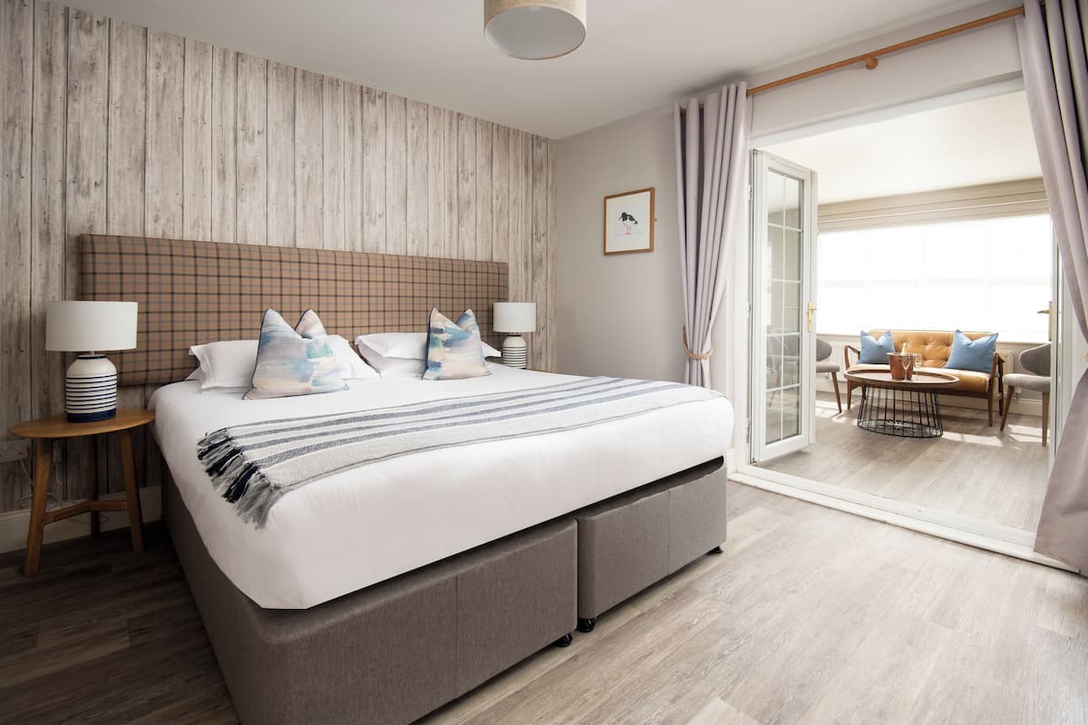 A bedroom with a large bed, two bedside tables, a view of the balcony, and a wooden wall.
