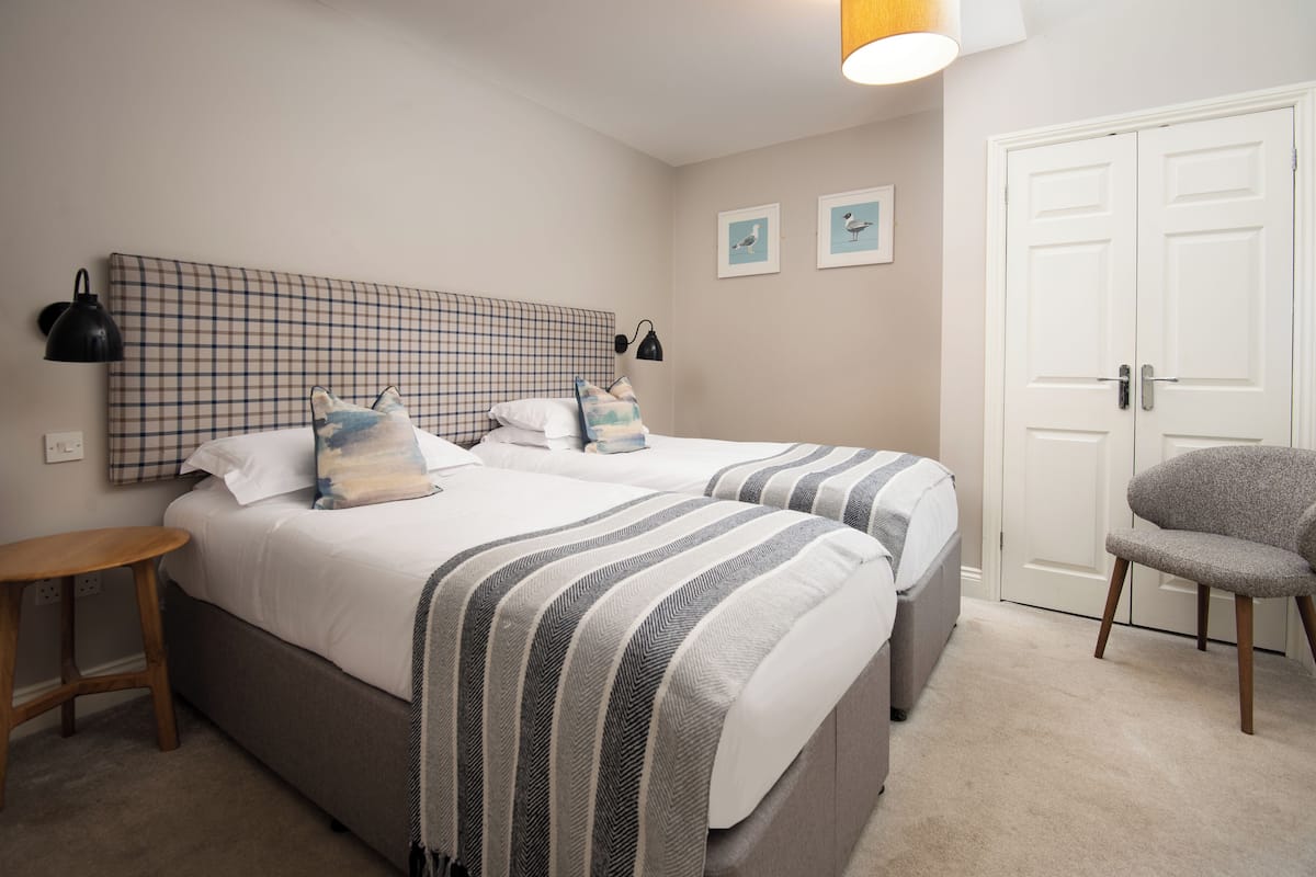 A bedroom with two beds, a chair, a lamp, and a door.