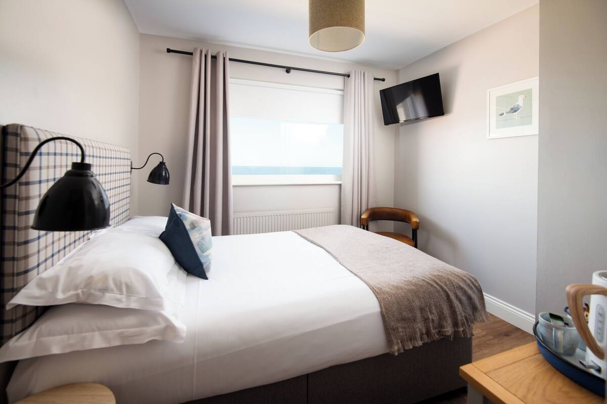 A neatly arranged bedroom with a bed, bedside lamps, a chair, a television, and a window with curtains.