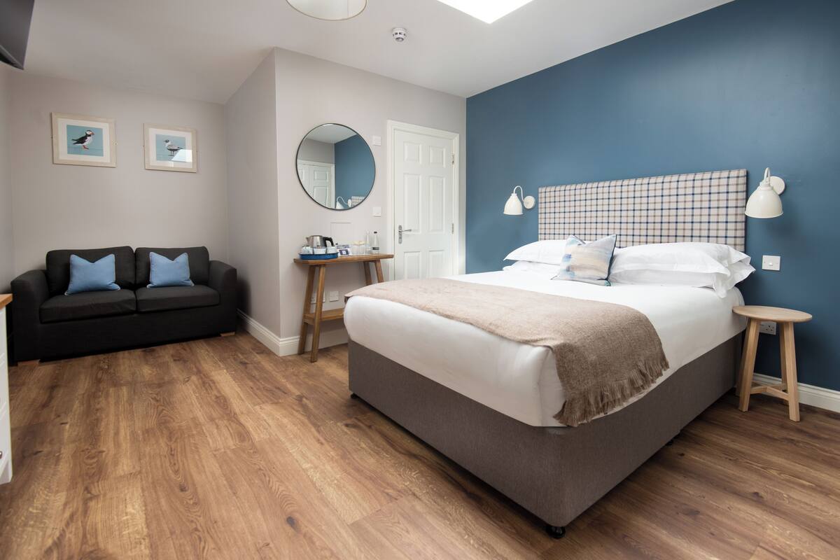 A bedroom with a bed, a sofa, a desk, and a mirror.