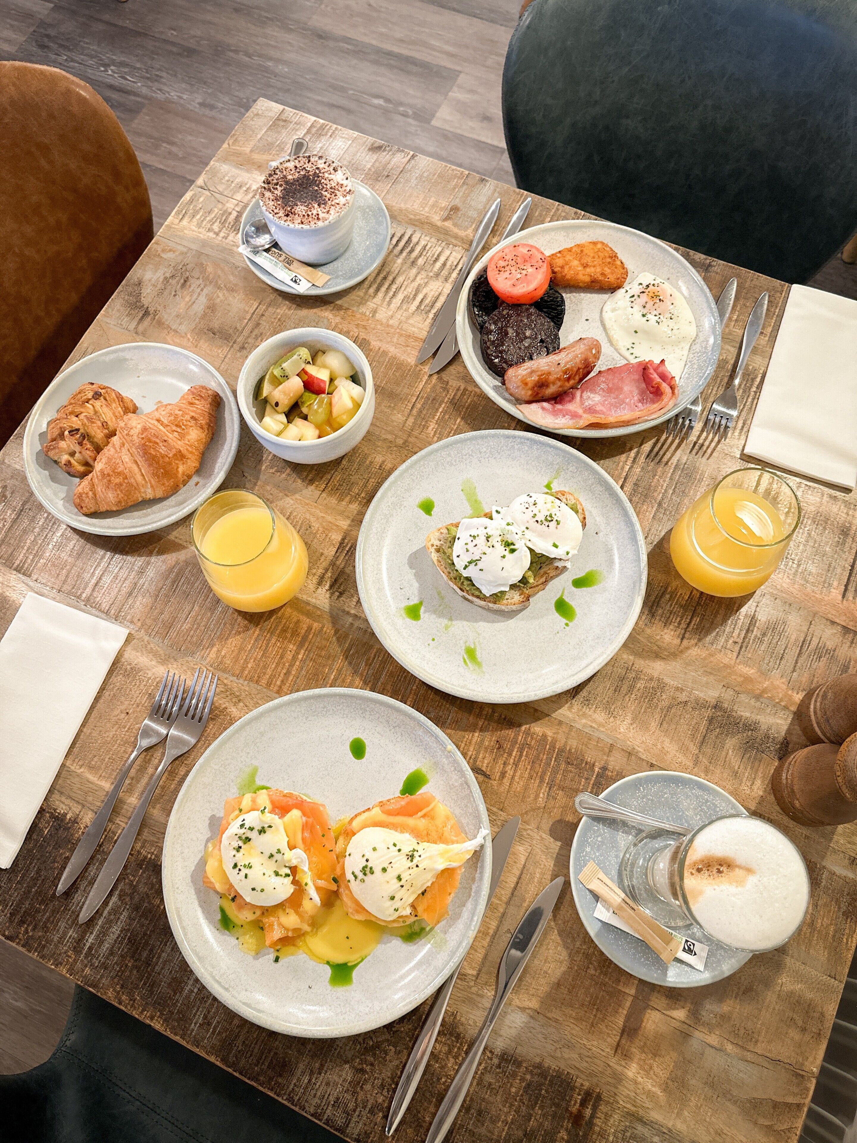 A breakfast setting with croissants, fruit salad, eggs, and coffee on a wooden table.
