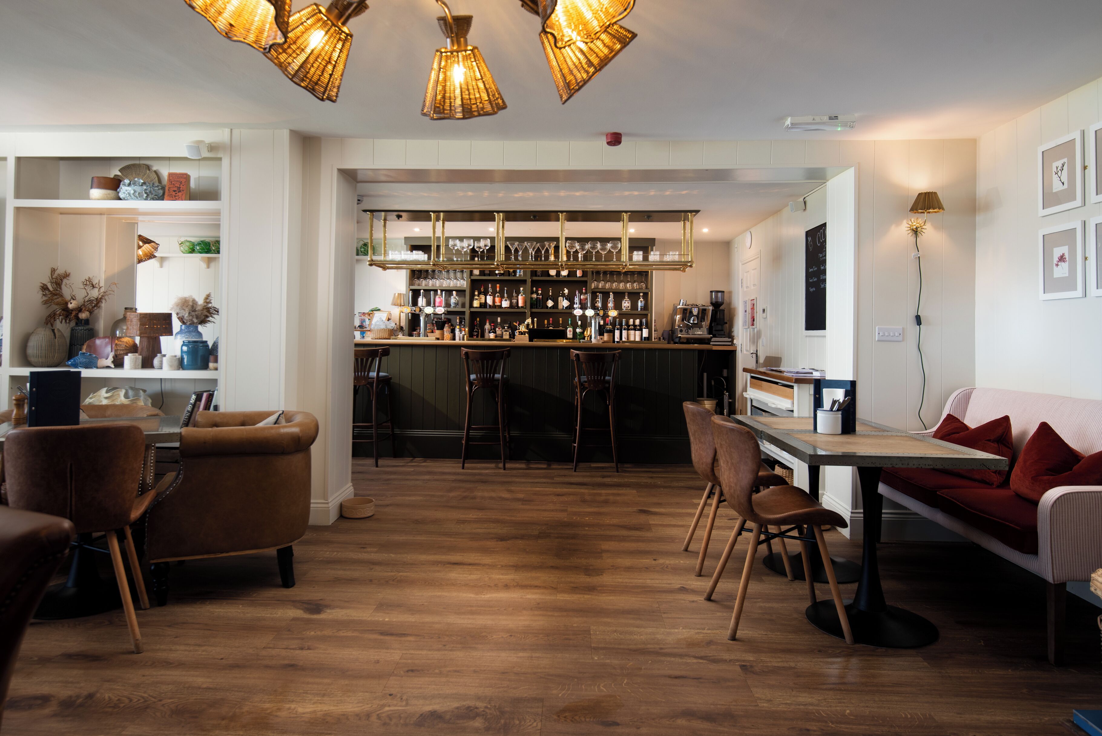 A bar area with wooden flooring, bar stools, and shelves with bottles and glasses.