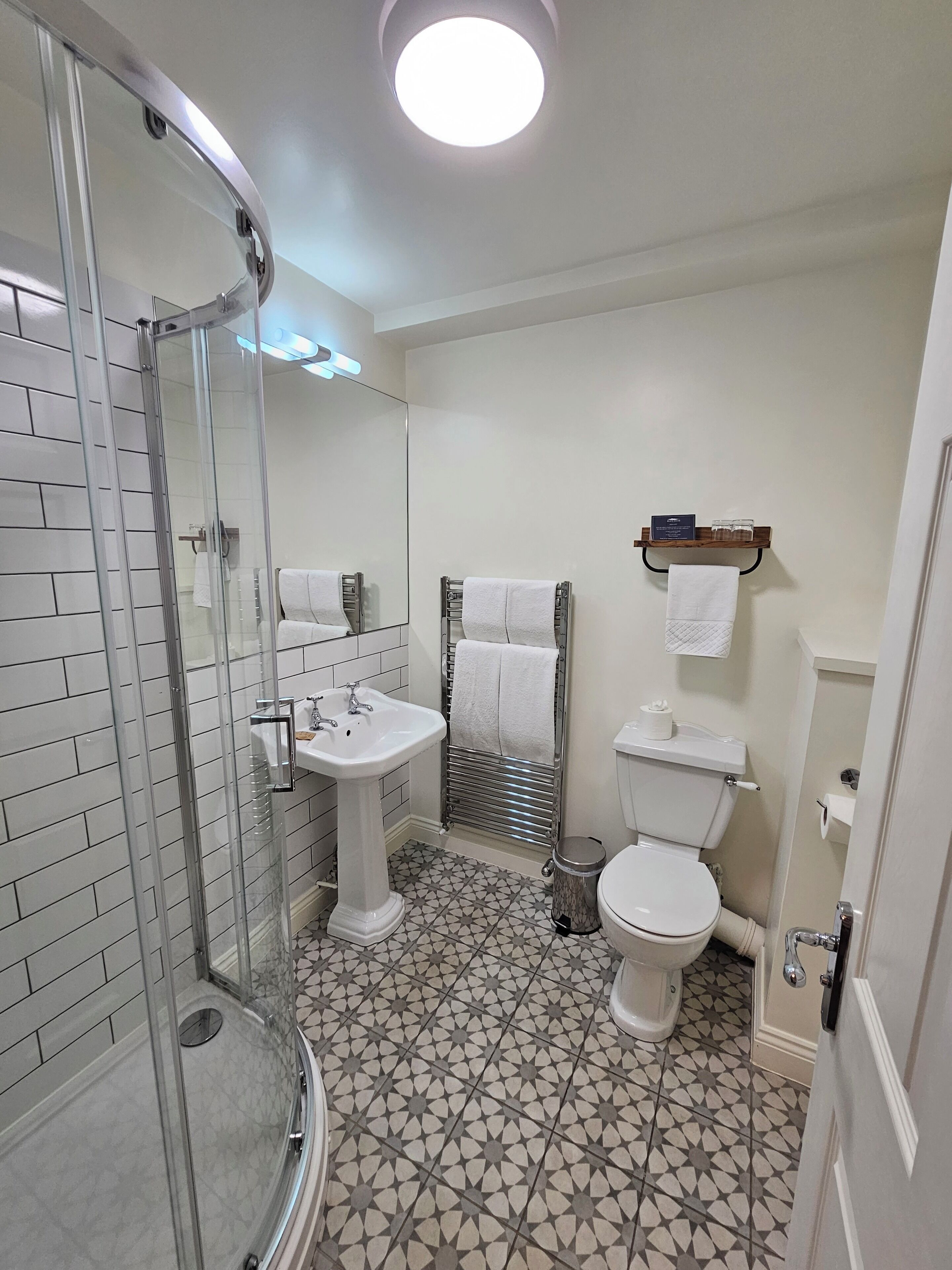 Une salle de bain avec une douche à parois de verre, un lavabo sur colonne, des toilettes et un carrelage au sol.