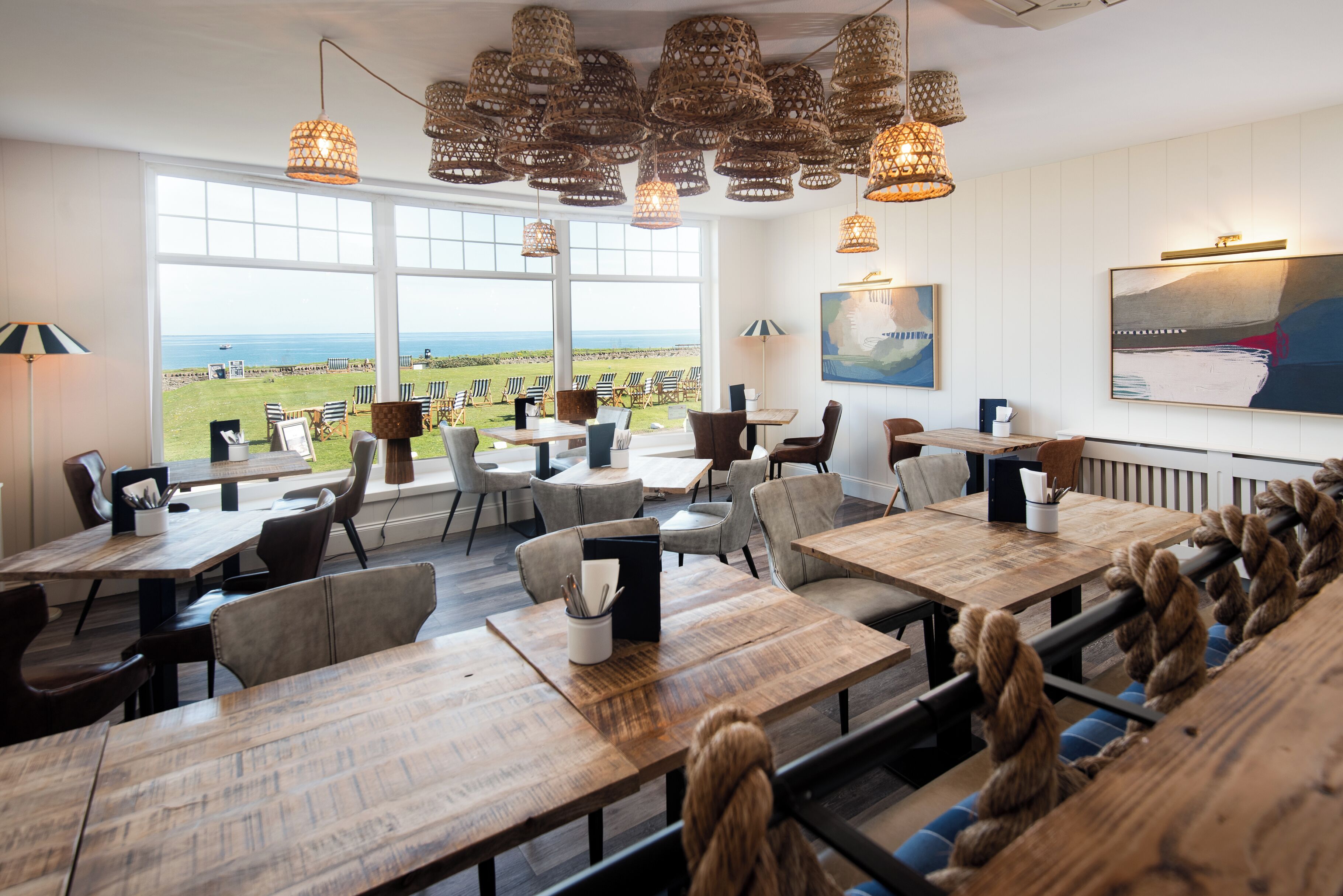 A restaurant with outdoor seating, large windows, and hanging wicker lamps.