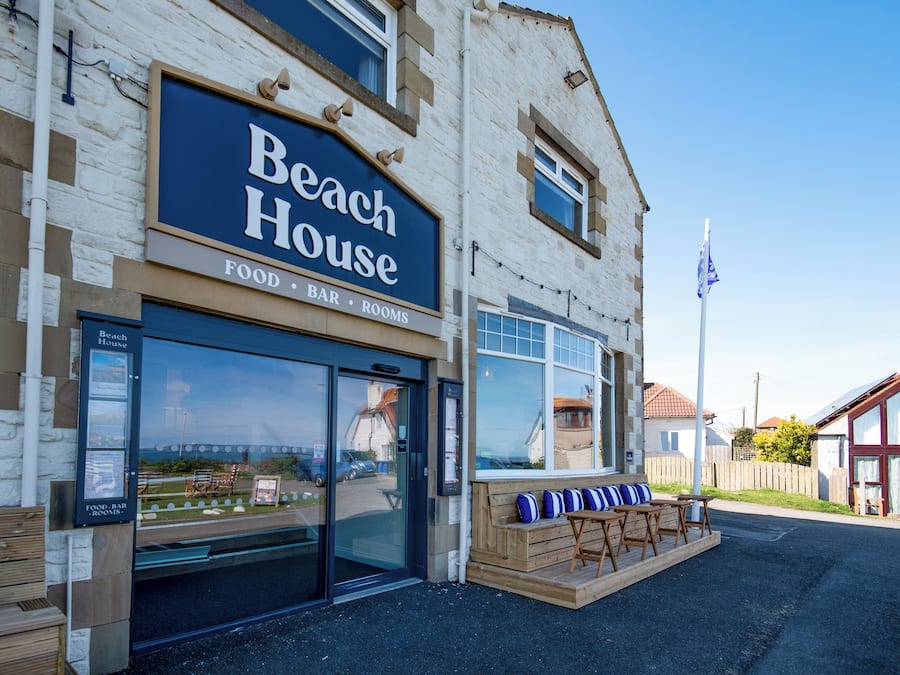 A building with a sign reading 'Beach House' and a view of the beach through the windows.