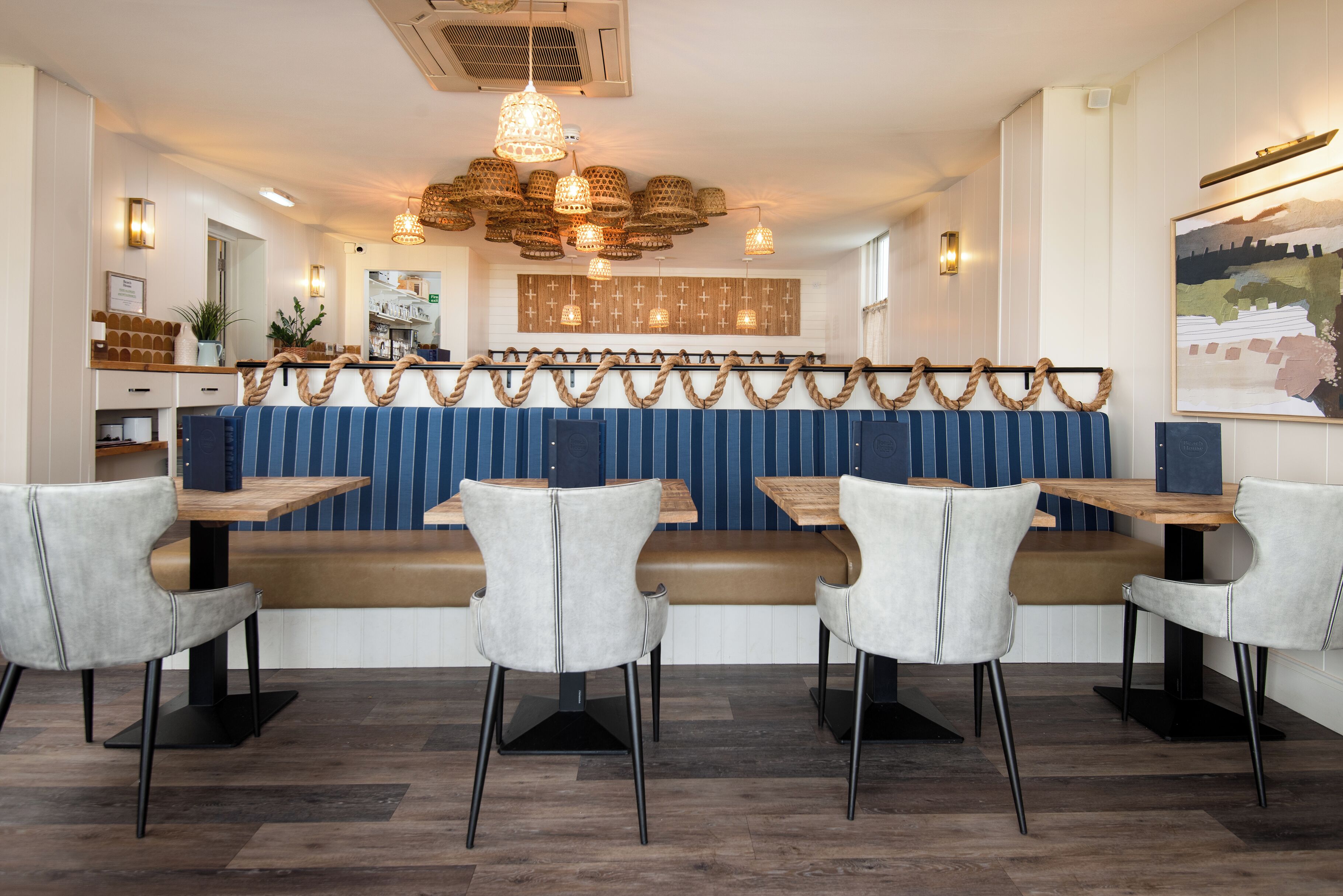 A restaurant interior with wooden tables, cushioned booths, and hanging pendant lights.