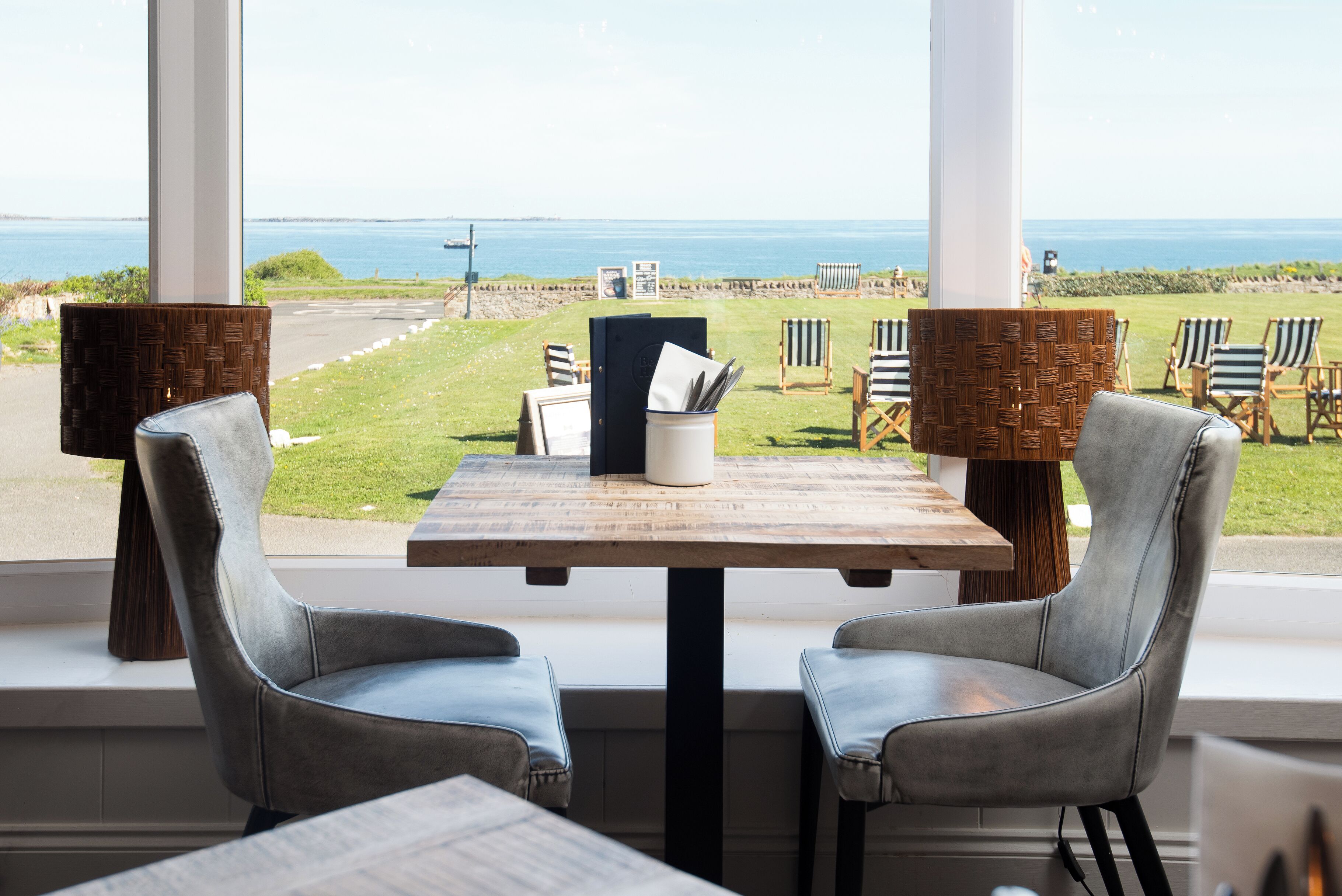 A table with two chairs, a menu, and a view of the ocean.