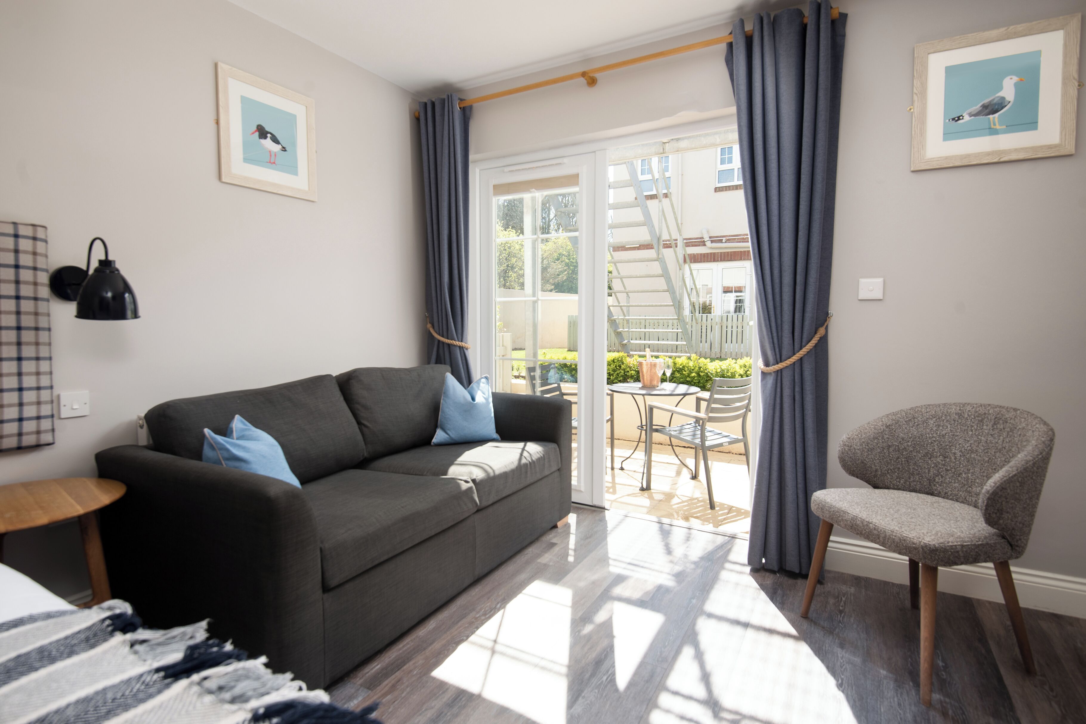 A modern living room with a sofa, a chair, a table, and a staircase leading to an outdoor area.